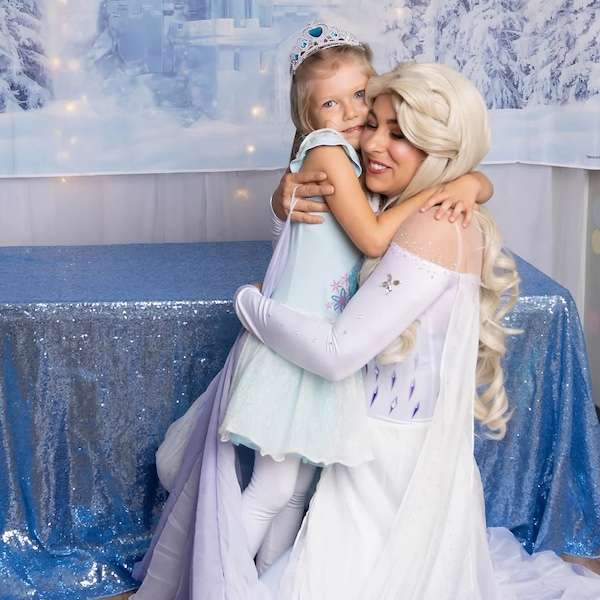 A performer dressed as an ice queen princess posing with a young child