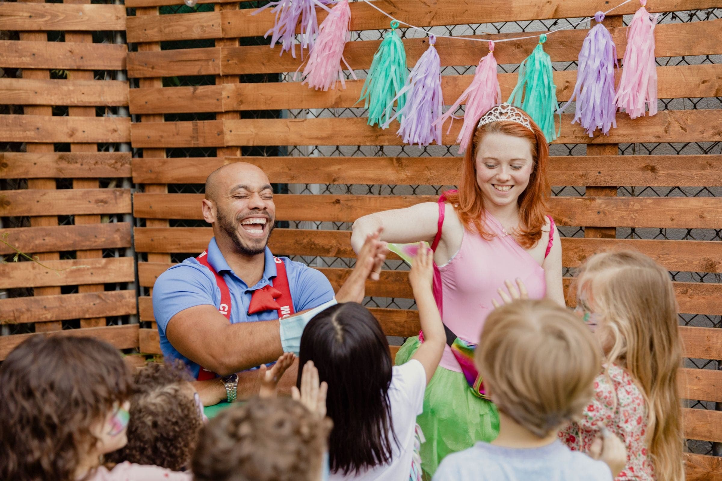 Two party entertainers high-fiving a group of excited children at a backyard party
