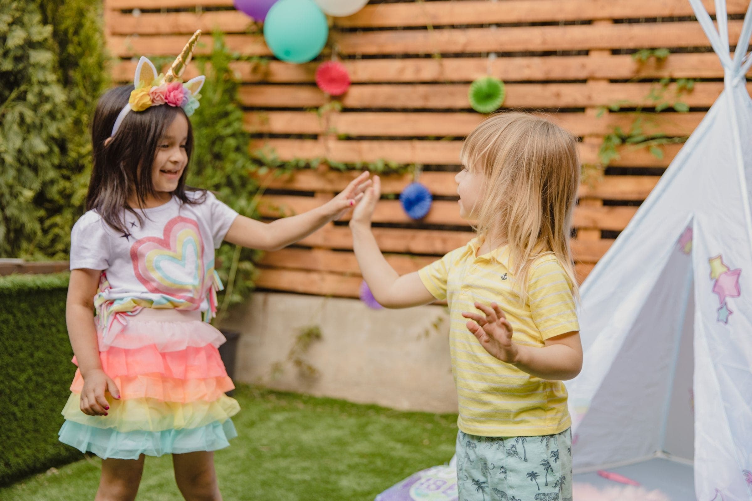 Two young children high-fiving each other on the lawn at a decorated backyard party