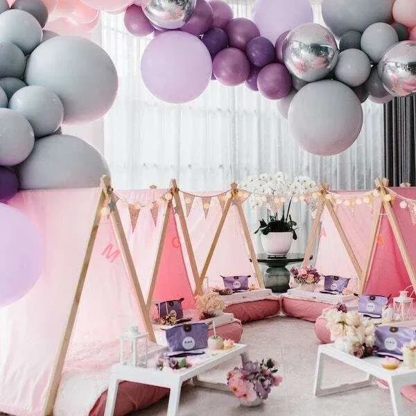 A pastel balloon garland over a party teepee setup
