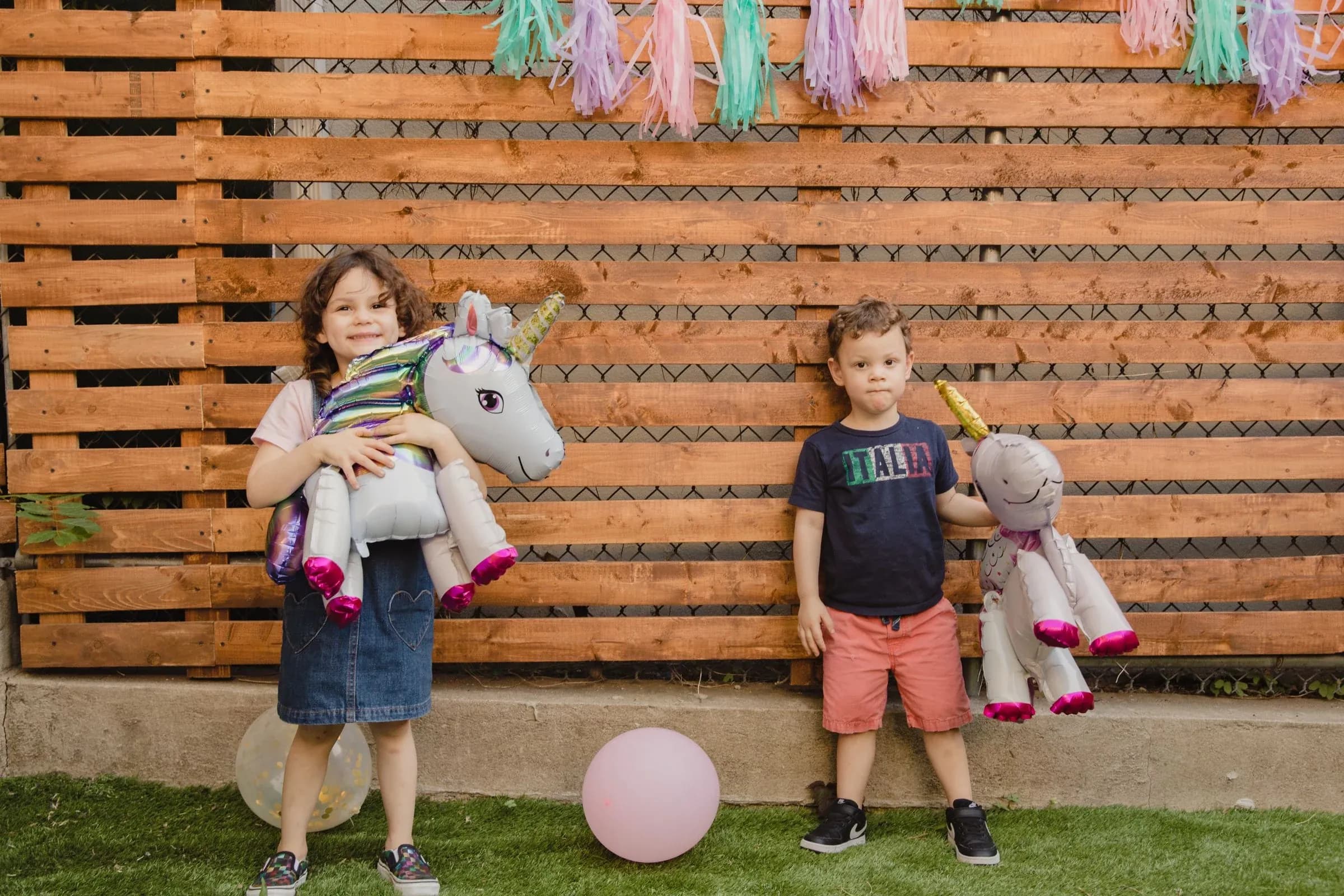 Two children holding unicorn balloons at a decorated backyard birthday party