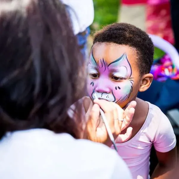 A face painter mid-brushstroke, working on a colorful design for a party guest